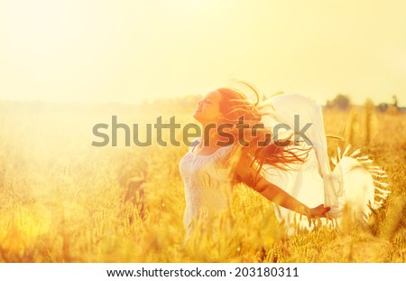 Beauty Girl Outdoors enjoying nature. Beautiful Teenage Model girl in white dress running on the Spring Field, Sun Light. Glow Sun. Free Happy Woman. Toned in warm colors