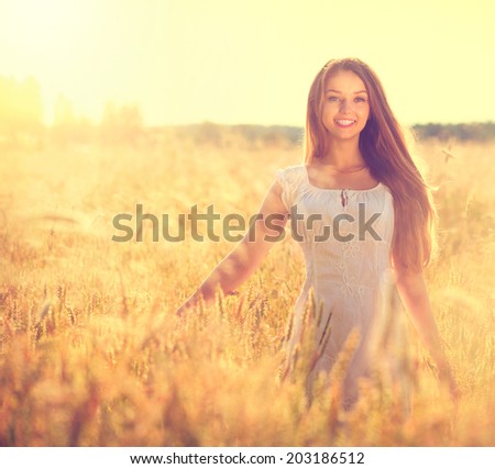 Beauty Girl Outdoors enjoying nature. Beautiful Teenage Model girl in white dress running on the Field, Sun Light. Glow Sun. Free Happy Woman. Toned in warm colors. Summer