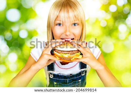 Girl eating Hamburger. Child with hamburger. Pretty little girl eating a sandwich over nature green bokeh background