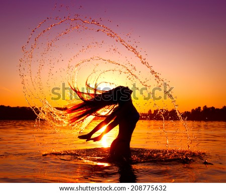 Beauty Model Girl Splashing Water with her Hair. Teen girl Swimming and splashing on summer beach over sunset. Beautiful Woman in Water