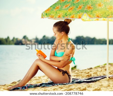 Suntan Lotion Woman Applying Sunscreen Solar Cream. Beautiful happy cute teen Girl applying Sun Tan Cream on her skin on the beach. Sun Tanning. Skin care and Protection. Vacation