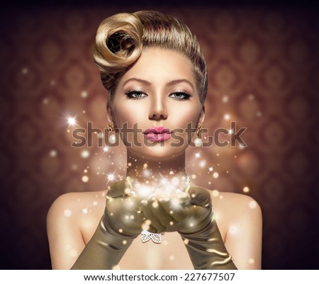 Holiday Retro Woman blowing magic dust in her hand. Beauty Fashion Christmas Vintage Style Lady with Beautiful Luxury Hairstyle, makeup, accessories. Golden Silk Gloves and dress