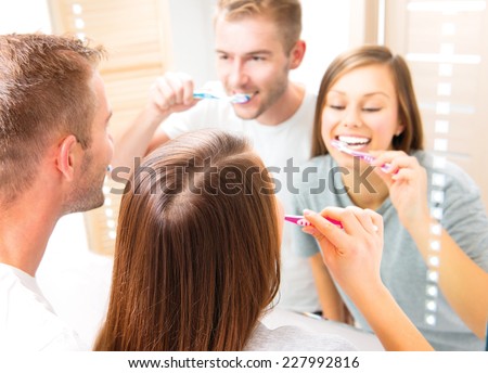 Beauty Young couple in the bathroom brushing teeth together. Happy family cleaning teeth with a tooth brush, looking at their white teeth at the mirror, enjoying their smile. Defocused reflection