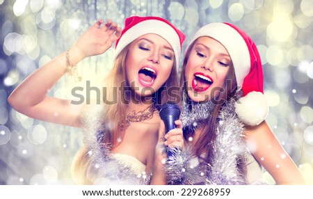 Christmas party, karaoke. Beauty girls in santa hat with a microphone singing and dancing over holiday blinking background. Disco. New year celebration