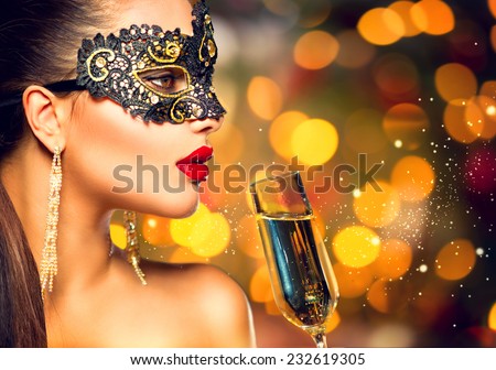 Sexy model woman with glass of champagne wearing venetian masquerade carnival mask at party, drinking champagne over golden holiday glowing background. Christmas, New Year celebration. Perfect make up