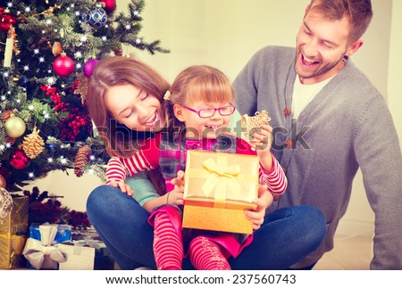 Christmas Family with little daughter opening Christmas gifts. Happy Smiling Parents and Child at Home Celebrating New Year. Christmas Tree. Christmas scene