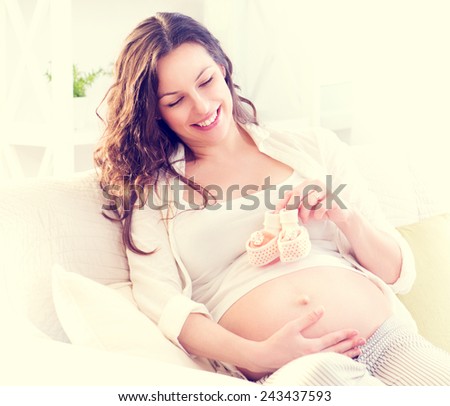 Pregnant Happy Woman holding blue Baby Shoes in her Hands. Mom Expecting Baby. Pregnant Woman Belly. Pregnancy. Baby Shower