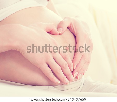 Pregnant Woman holding her hands in a heart shape on her baby bump. Pregnant Belly with fingers Heart symbol. Maternity concept. Baby Shower. Motherhood