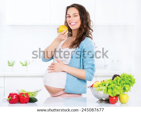 Pregnant Young Woman eating apple. Cooking vegetables. Healthy Food - Vegetable Salad. Diet. Dieting Concept. Healthy Lifestyle. Cooking At Home. Prepare Food
