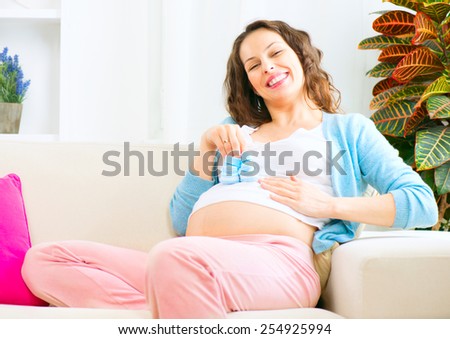 Pregnant Happy Woman holding blue Baby Shoes in her Hands. Mom Expecting Baby boy. Pregnant Woman Belly. Pregnancy. Baby Shower