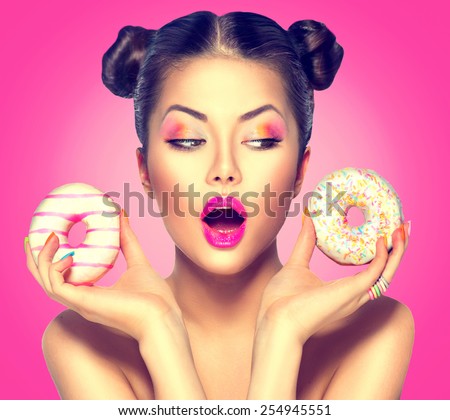 Beauty fashion model girl taking sweets and colorful donuts. Funny joyful Vogue styled woman choosing sweets on pink background. Diet, dieting concept. Junk food, Slimming, weight loss