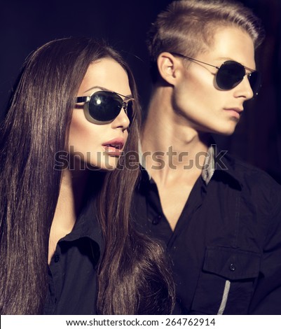 Fashion models couple wearing sunglasses. Sexy woman and handsome young man portrait over dark background. Attractive fashion Boy and girl posing. Hairstyle, haircut