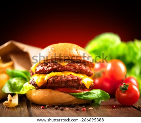 Hamburger with fries on wooden table. Cheeseburger on fresh buns with succulent beef patties and fresh salad ingredients served with French Fries on crumpled brown paper on a rustic wood table
