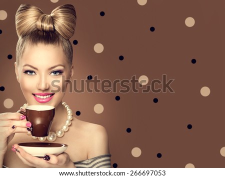 Beauty fashion model girl drinking coffee or tea. Beautiful young woman with cup of hot beverage. Retro styled vintage lady with professional make up, funny bow hair style. Polka dots brown background