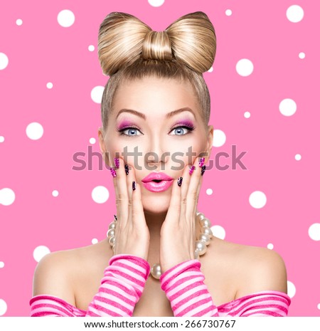 Beauty Surprised fashion model girl with funny bow hairstyle, pink nail art and makeup over polka dots background. Colourful Studio Shot of Funny Woman. Vivid Colors. Emotion
