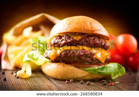 Hamburger with fries on wooden table. Cheeseburger on fresh buns with succulent beef patties and fresh salad ingredients served with French Fries in crumpled brown paper on a wooden table