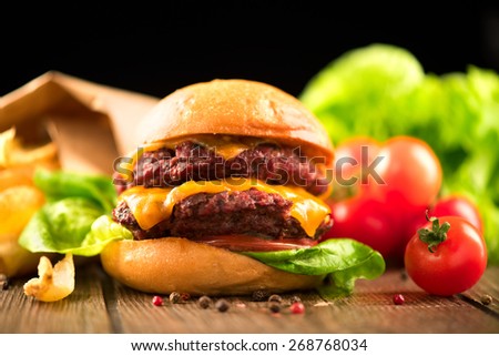 Hamburger with fries on wooden table. Cheeseburger on fresh buns with succulent beef patties and fresh salad ingredients served with French Fries on a wooden table