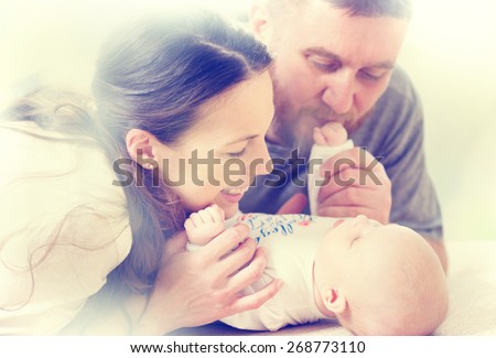 Father, Mother and their Newborn Baby. Happy Family - Mom, Dad and Baby kissing and hugging. Resting in bed together. Parenthood concept.
