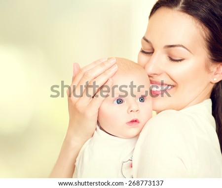 Mother and her Newborn Baby. Happy Mother and Baby kissing and hugging. Resting in bed together. High key soft image of Beautiful Family. Maternity concept. Parenthood. Motherhood