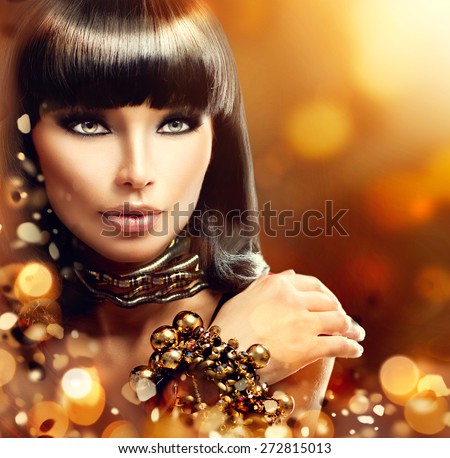 Fashion model brunette girl with golden accessories over gold shiny background. Golden Jewellery. Gold Jewelry. Beauty Egyptian Style Woman with Gold Accessories. Golden bracelet and Necklace