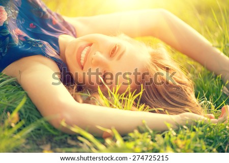 Beautiful Young Woman lying on the field in green grass and laughing. Outdoors. Enjoy Nature. Healthy Smiling Girl on spring lawn