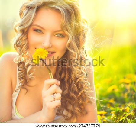 Beauty blond model girl lying on a field and smelling dandelion flowers. Allergy free. Beautiful Young Woman in the Meadow.  Outdoors. Enjoy Nature. Healthy Smiling Girl portrait