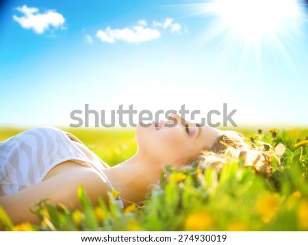 Beautiful Healthy Girl lying on summer field with flowers. Outdoors. Enjoy Nature. Healthy Smiling Girl on spring lawn. Allergy free concept. Freedom. Happy person outdoor