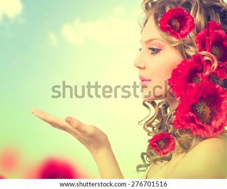 Beauty girl with red poppy flowers hairstyle and open hands. Blowing flower. Hairstyle with flowers. Fantasy girl portrait over blue sky outdoor. Summer fairy portrait. Long permed hair