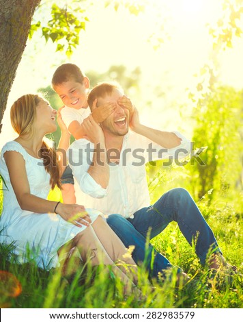 Happy joyful young family father, mother and little son having fun outdoors, playing together in summer park. Mom, Dad and kid laughing and hugging, enjoying nature outside. Sunny day, good mood