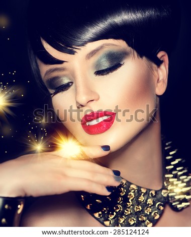 Beauty Fashion Model Girl with bright Makeup and golden Accessories. Rocker Style Brunette Portrait. Short haircut. Fringe Hairstyle. Rocker or Punk sexy Woman. Isolated on black background. Hair cut