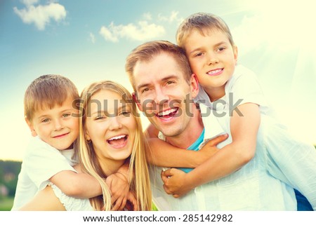 Happy joyful young family father, mother and kids having fun outdoors, playing together outside. Mom, Dad and kid laughing and hugging, enjoying nature. Sunny day, good mood