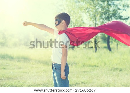 Super Hero Kid having fun outdoor. Superhero little boyover nature green blurred background