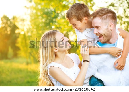 Happy joyful young family father, mother and little son having fun outdoors, playing together in summer park, countryside. Mom, Dad and kid laughing and hugging, enjoying nature outside. Piggyback
