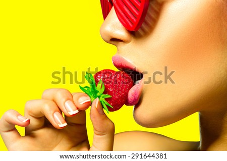 Sexy Woman wearing red Glamor sunglasses Eating Strawberry. Sensual Lips. Over vivid yellow background. Bright Manicure and Lipstick. Desire. Beauty Girl Sexy Lips with Strawberry