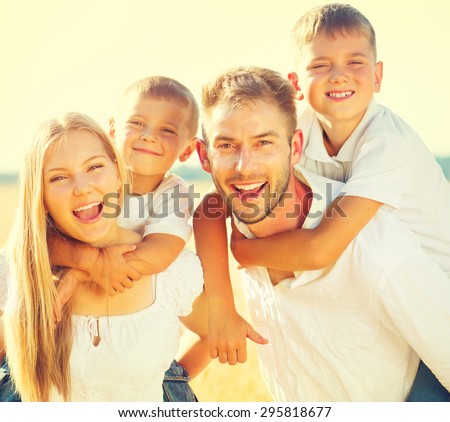Happy Young Family with two children walking on wheat summer field. Healthy mother, father and little sons enjoying nature together, outdoors. Healthy Smiling Dad, Mom and kids together. Harvest