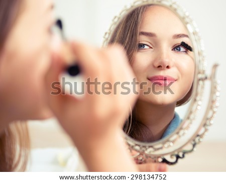 Beauty model teenage girl looking in the mirror and applying mascara make up. Beautiful young woman apply makeup