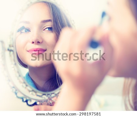 Beauty model girl looking in the mirror and applying mascara make up. Beautiful young woman apply makeup