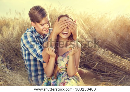 Beauty Couple relaxing on wheat field together. Teenage girlfriend and boyfriend having fun outdoors, kissing and hugging, first love concept. Teenagers Boy and Girl in love together