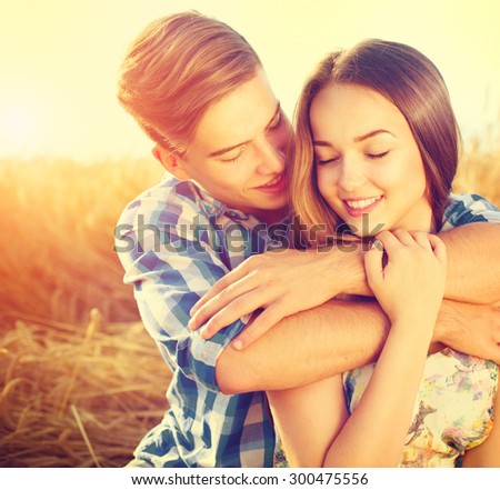 Beauty Couple relaxing on wheat field together. Teenage girlfriend and boyfriend having fun outdoors, kissing and hugging, love concept. Teenagers Boy and Girl in love together