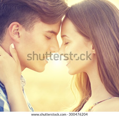 Beauty Couple relaxing on wheat field together. Teenage girlfriend and boyfriend having fun outdoors, kissing and hugging, first love concept. Teenagers Boy and Girl in love together