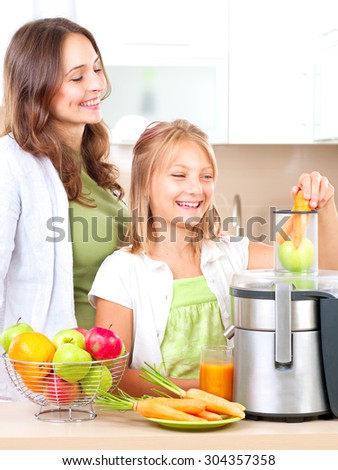 Happy Family making fresh apple and carrot juice. Smiling Mother and her daughter Girl drinking fresh carrot and apple juice. Juice Extractor. Healthy eating concept, vitamins.