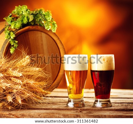 Beer barrel and two beer glasses with green hop and ears of wheat on wooden table. Dark and light beer. Brewery concept. Brewing traditions