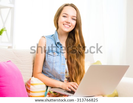 Young smiling girl sitting on the sofa and using laptop at home. Teenage girl with laptop, smiling and looking in camera. Teenager with laptop. education concept. Working Online