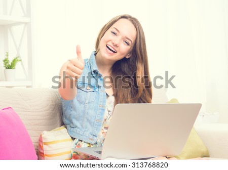 Pretty teenage girl sitting on sofa at home with her laptop, making thumb up gesture. Beauty girl with laptop computer Vintage style. Smiling and laughing