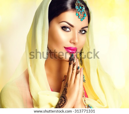 Beauty Indian girl with mehndi tattoos hold palms together. Beautiful Hindu exotic woman in sari and emerald oriental jewels looking in camera. India. Traditions concept