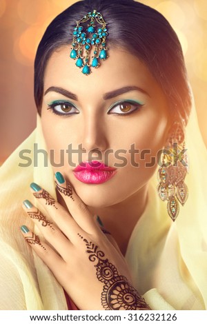 Beauty Indian woman portrait. Brunette Hindu model girl with brown eyes, mehendi tattoo on her hand and national Indian jewels looking in camera. Indian girl in sari. Traditions
