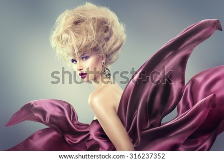 High fashion model girl portrait. Glamorous beauty woman with Updo hairstyle and bright makeup dressed in violet silk flying dress. Glamour Lady posing in studio