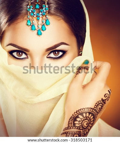 Beautiful Indian girl with traditional turquoise jewels hiding her face behind the veil. Young Hindu woman portrait with mehndi tattoos from black henna on hand. Beauty Arabian model looking at camera