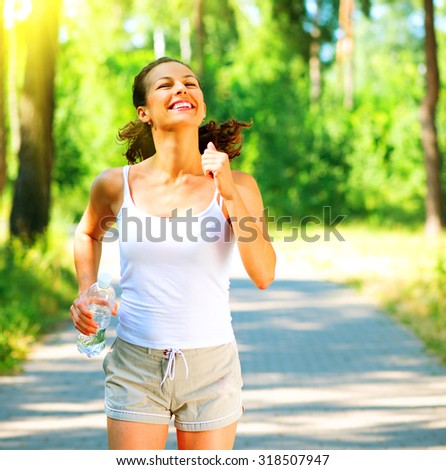 Woman running with bottle of water. Young sporty lady jogging outdoor in the park. Brunette model enjoy the training Workout. Exercises. Healthy lifestyle.
