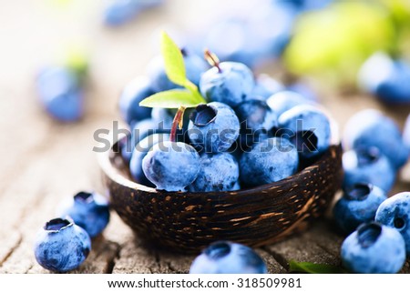 Blueberries in wooden bowl over rustic wooden table close up. Ripe and juicy fresh picked blueberry with green leaves. Berries harvest. Bilberries over wooden background. Berries. Diet concept